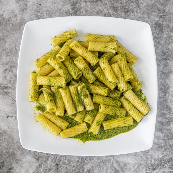 A white square plate filled with rigatoni pasta coated in vibrant green pesto sauce.