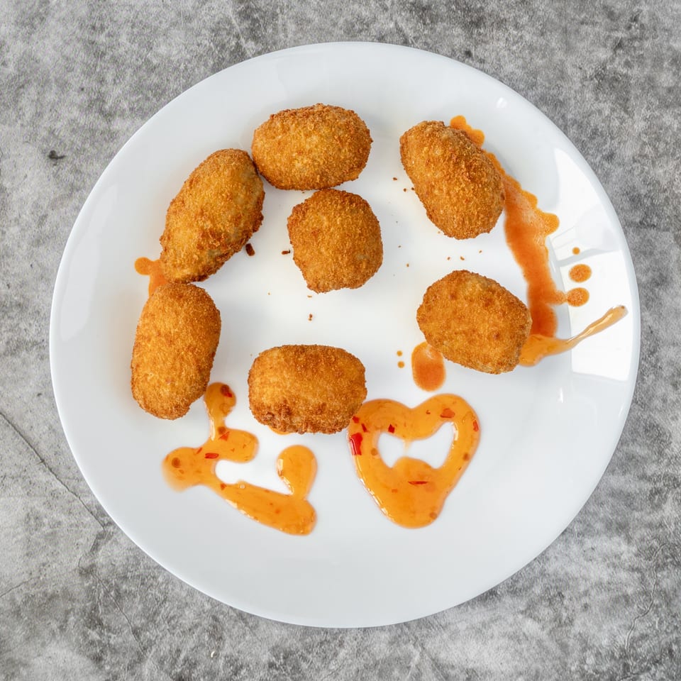 Seven golden-brown fried arancini balls with sweet chili sauce on a white plate.