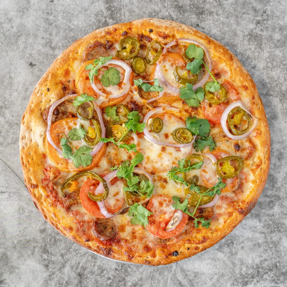 Ameci Pizza & Pasta's pizza with tomatoes, onions, jalapeños, and cilantro on a gray surface.