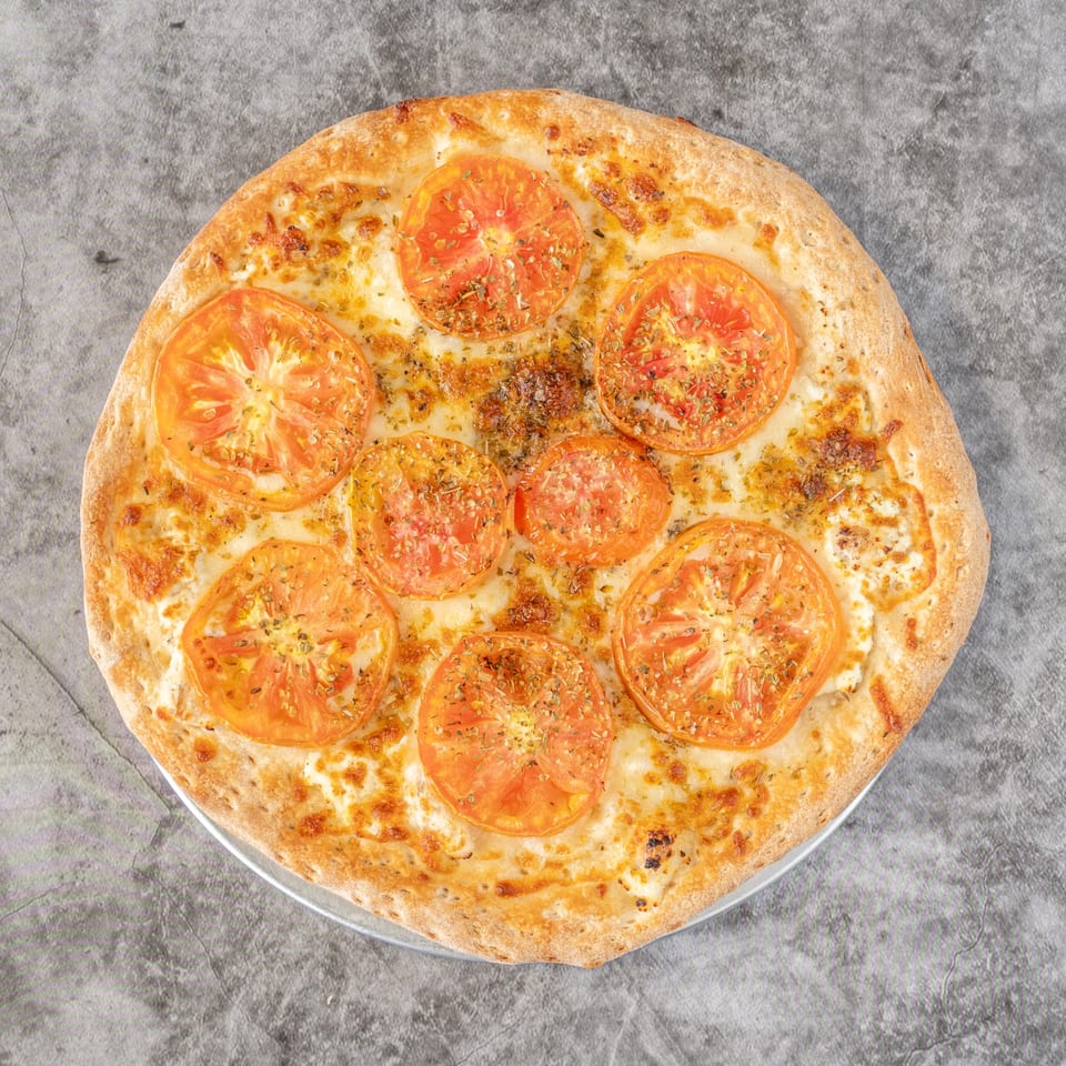 Ameci Pizza & Pasta's white pizza with sliced tomatoes and herbs on a gray surface.