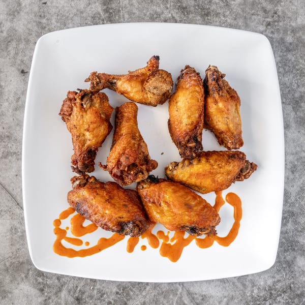 Crispy fried chicken wings and drumettes with a drizzle of orange sauce on a white plate.