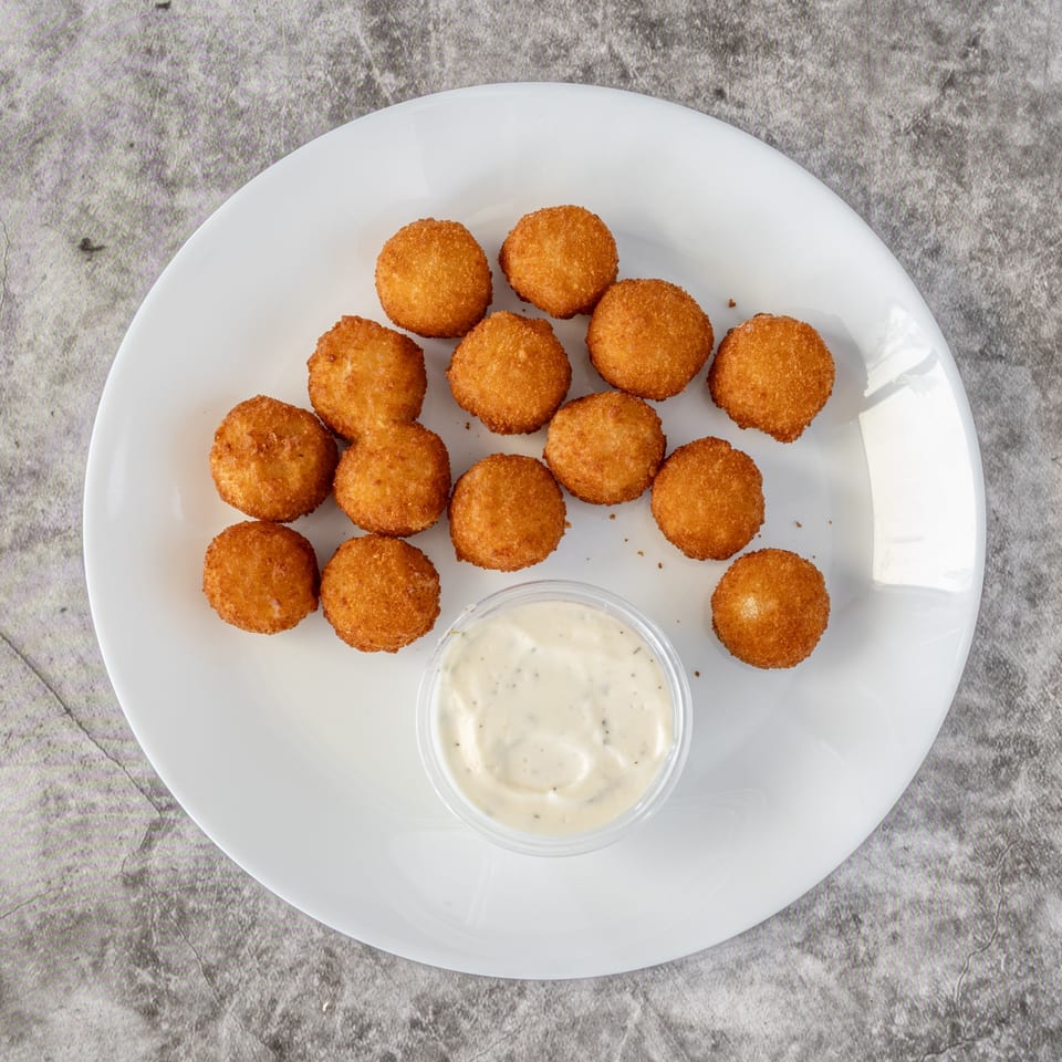 Golden-brown fried cheese balls and a small cup of dipping sauce on a white plate.