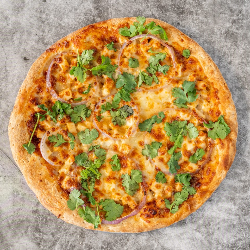 Ameci Pizza & Pasta's BBQ chicken pizza with red onions and cilantro on a gray background.